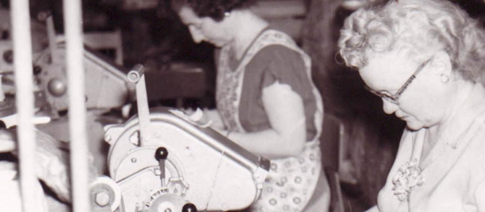 Archival photo: two women assembling components at factory workstations